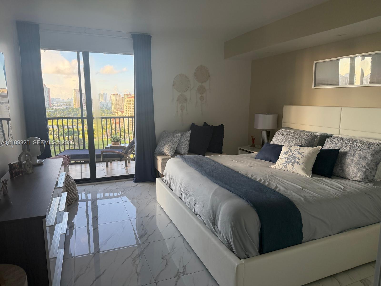 Polished stone-finish flooring with marbled veining, floor-to-ceiling sliding glass doors, and a covered balcony featuring a metal railing