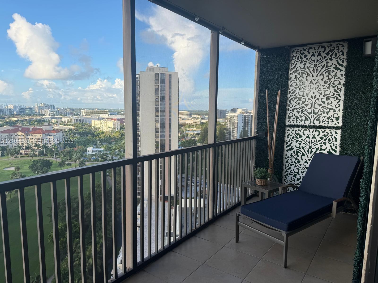 Screened balcony featuring dark metal railings and tile flooring with panoramic scenery of a golf course and a city skyline