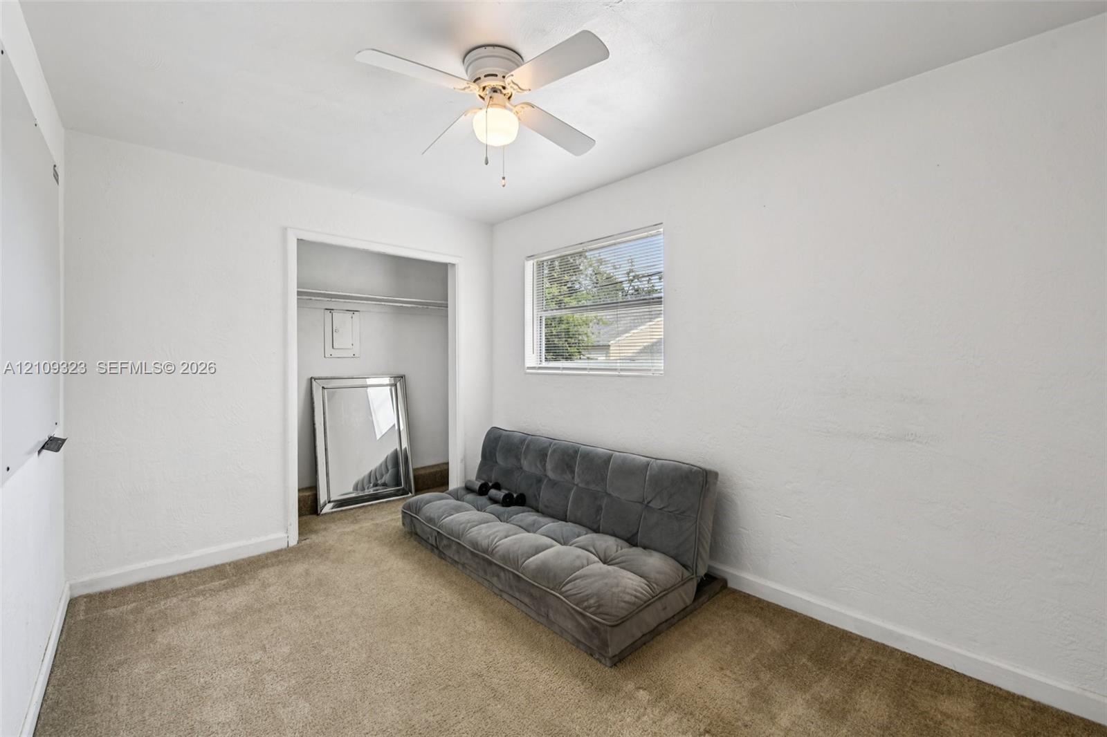 Neutral-toned carpeting, ceiling fan with integrated lighting, reach-in closet with built-in shelf, and a rectangular window