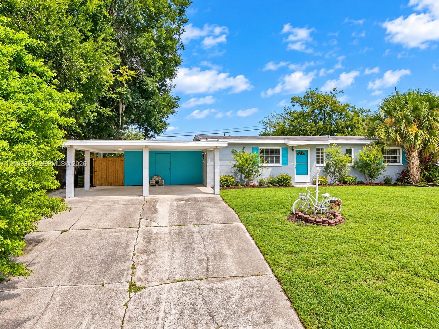 Single-story residence featuring a covered carport, concrete driveway, front lawn, and exterior shutters Single-story residence featuring a covered carport, concrete driveway, front lawn, and exterior shutters