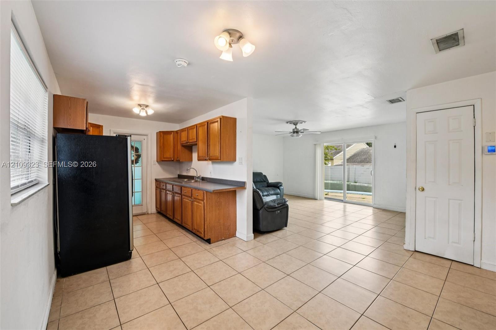 Kitchen featuring wood cabinetry, solid-surface countertops, tile flooring, dual-light ceiling fixtures, and glass-paneled sliding doors