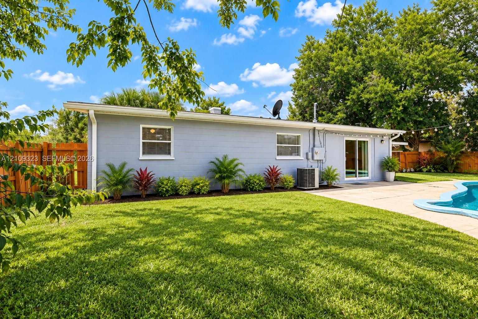 Expansive backyard featuring a swimming pool, concrete patio, perimeter wood fencing, and mature landscaping