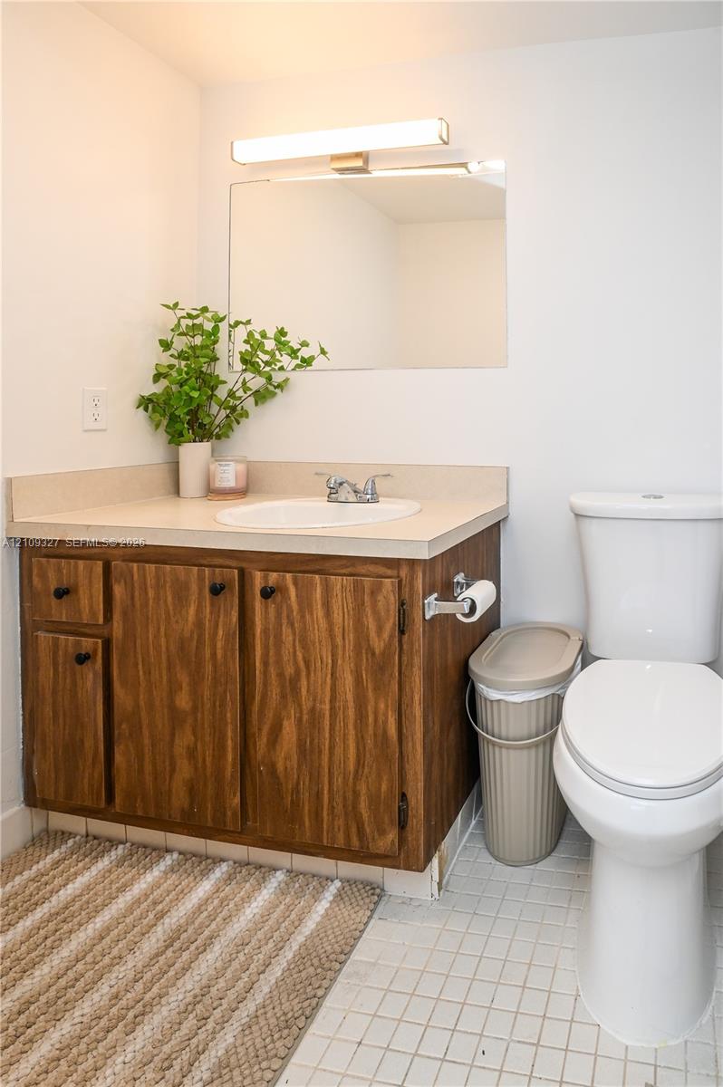 Bathroom featuring a wood-finish vanity cabinet, light-toned solid surface countertop, integrated oval sink, frameless wall-mounted mirror, and linear light fixture