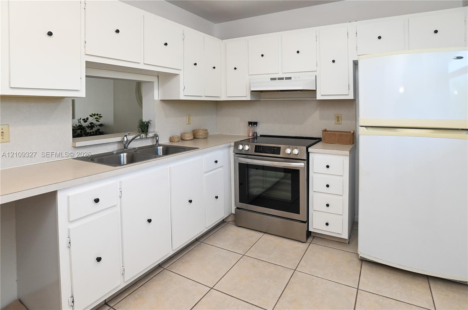 Kitchen featuring white cabinetry, stainless steel range, dual-basin sink, laminate countertops, and tile flooring