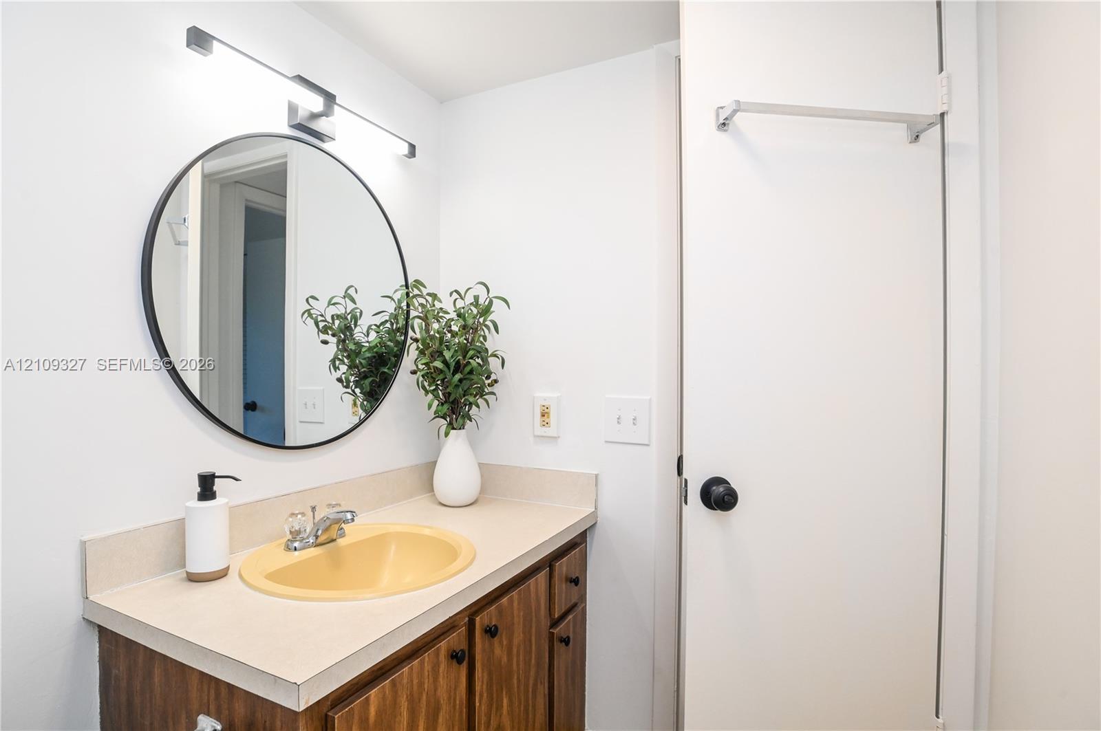 Vanity featuring a wood-finish cabinet, solid-surface countertop, integrated basin, circular wall-mounted mirror, and linear vanity light fixture