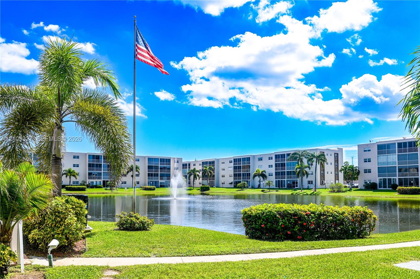 Waterfront grounds featuring a central pond with a fountain, manicured landscaping, mature palm trees