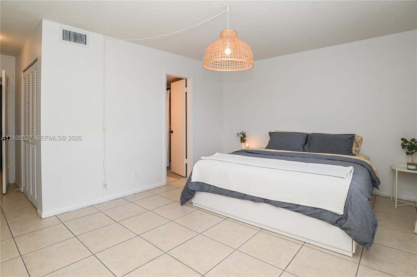 Neutral-toned ceramic tile flooring, textured ceiling, and louvered closet doors