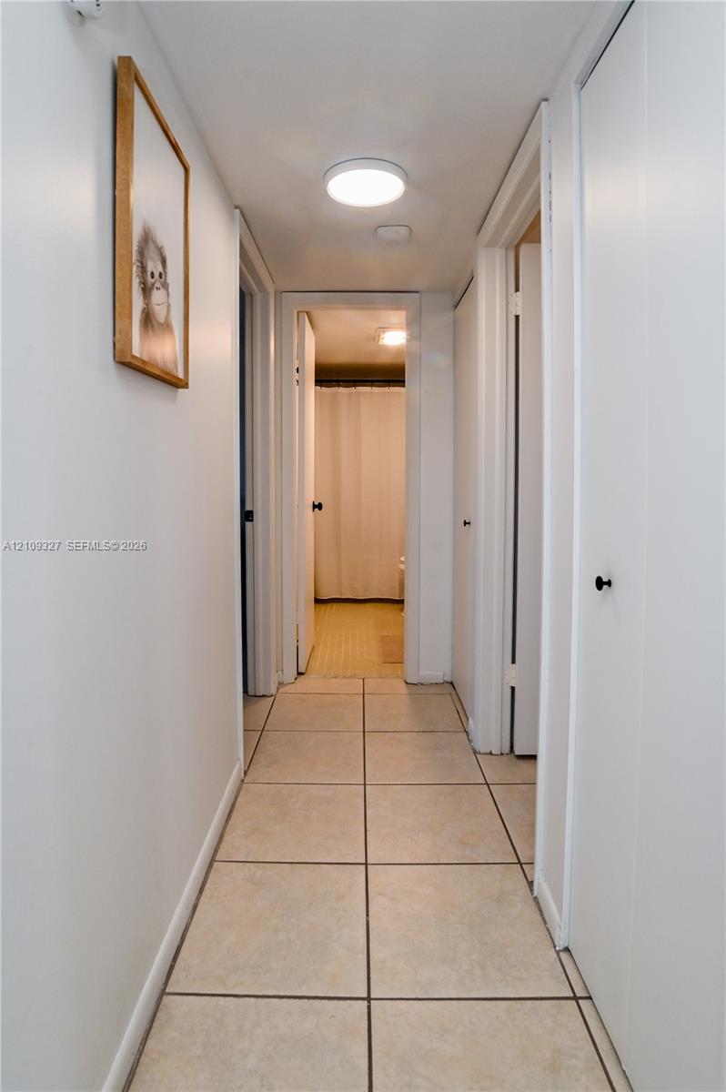 Hallway featuring neutral-toned tile flooring, flush-mount lighting, and multiple interior doors