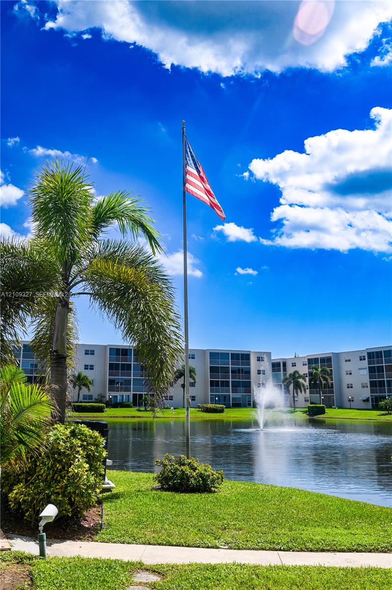 Waterfront exterior featuring a central fountain, manicured lawn, established palm trees, and a flagpole
