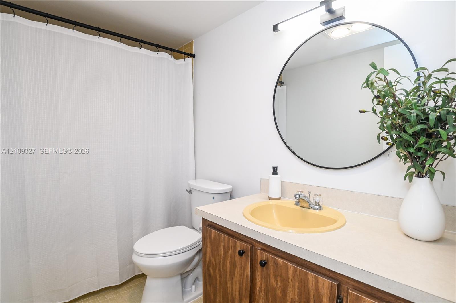 Bathroom featuring a wood-finish vanity with a molded basin, round wall-mounted mirror, and linear light fixture