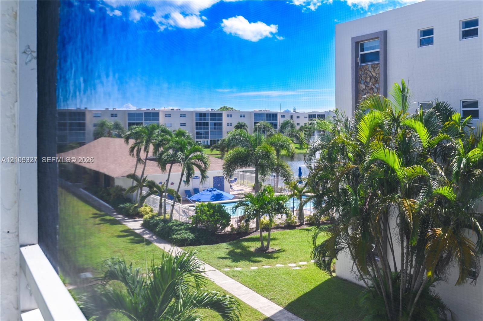 Outdoor space featuring a swimming pool, paved walkways, mature palm trees, and a water feature