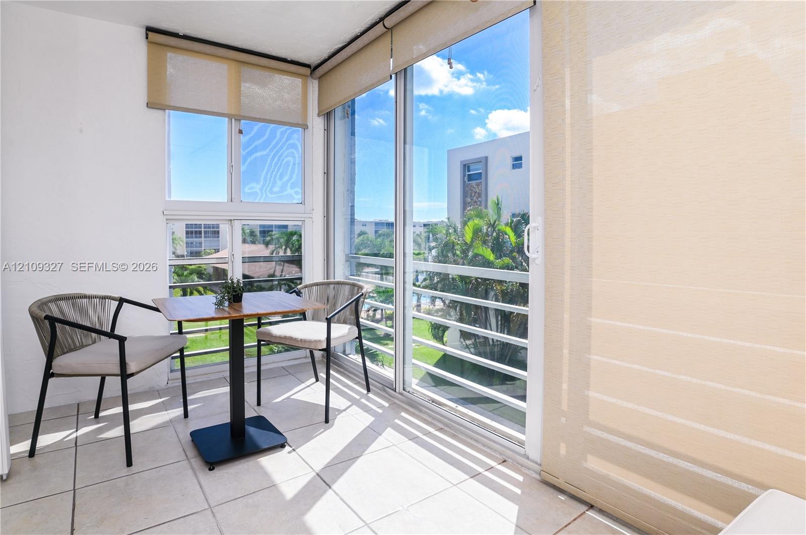 Balcony featuring large-format ceramic floor tiles, expansive floor-to-ceiling glass sliding doors, and windows with neutral roller shades