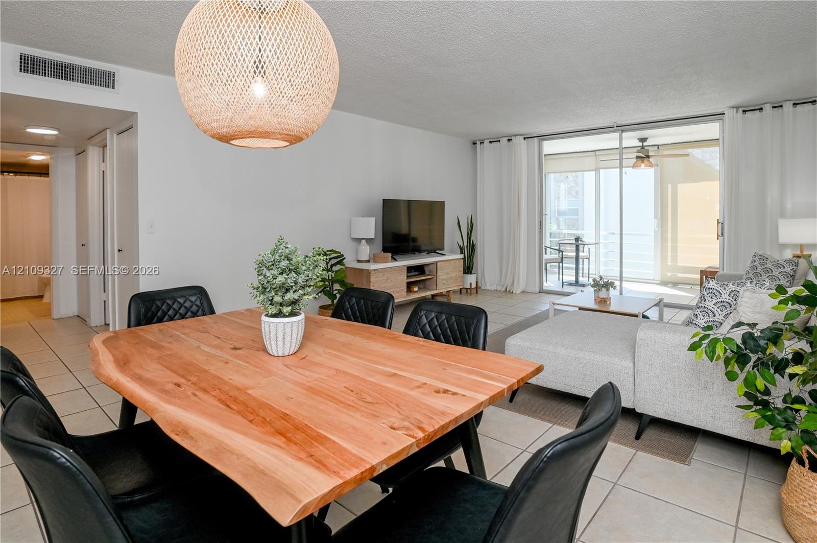 Open-concept living space featuring large-format tile flooring, a woven dome pendant light fixture, and floor-to-ceiling sliding glass doors providing outdoor access