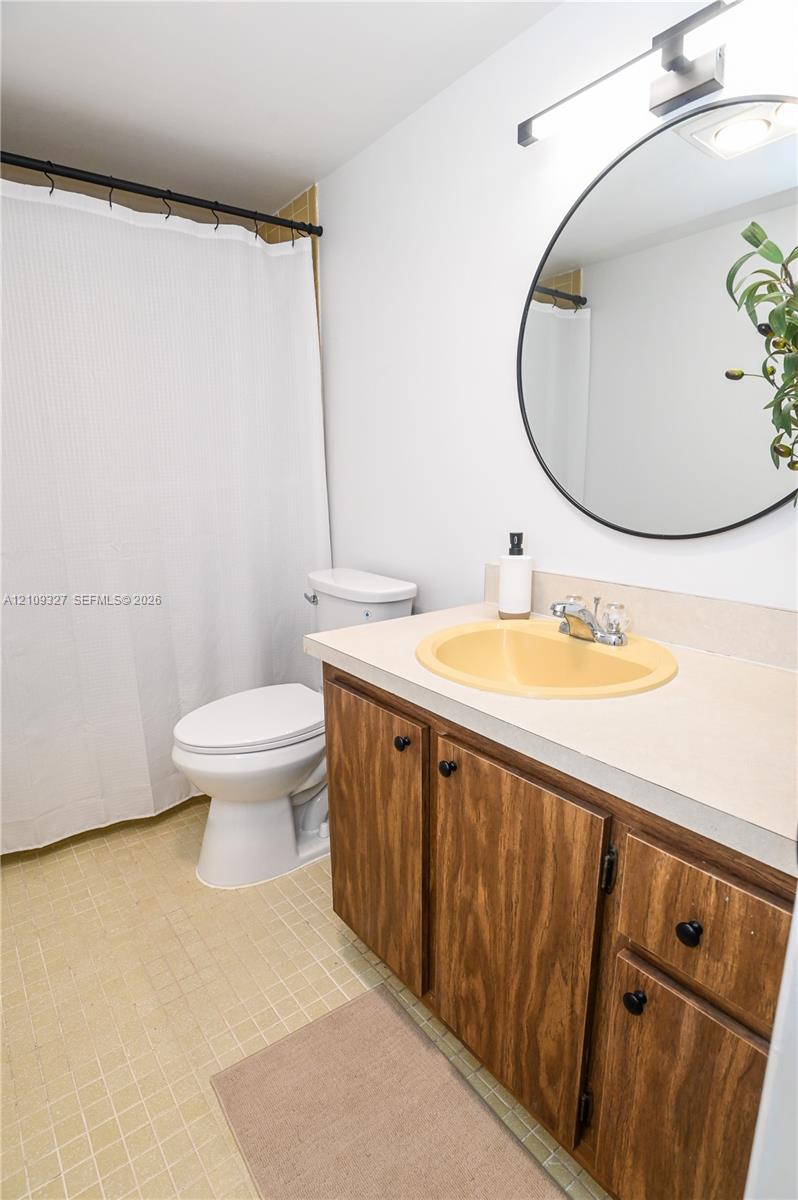 Vanity featuring wood-finish cabinetry, a neutral countertop with an integrated basin, circular wall-mounted mirror, and horizontal linear light fixture