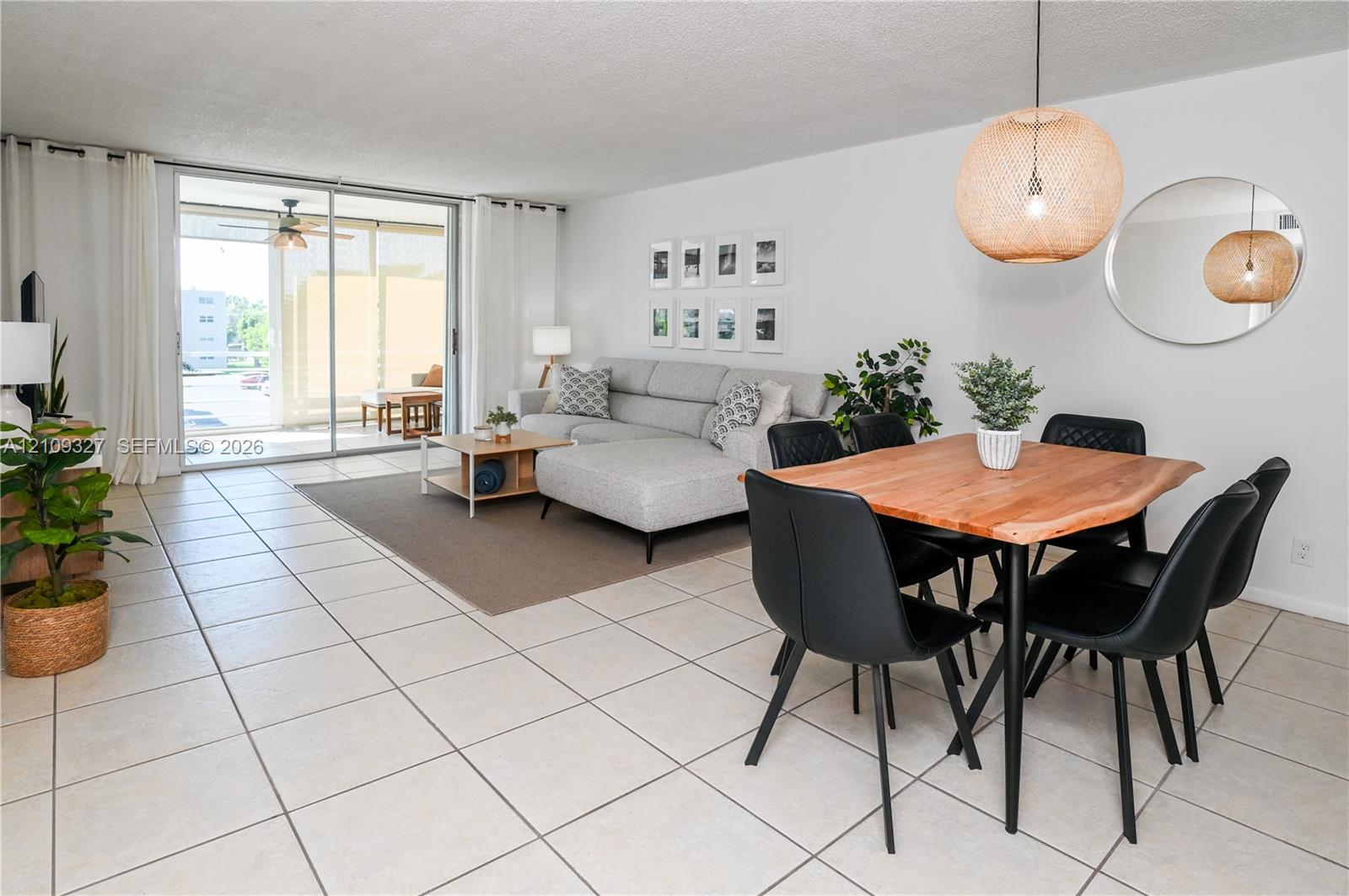 Open-concept living space featuring large-format ceramic tile flooring, sliding glass door, woven pendant lighting, and a circular wall-mounted mirror