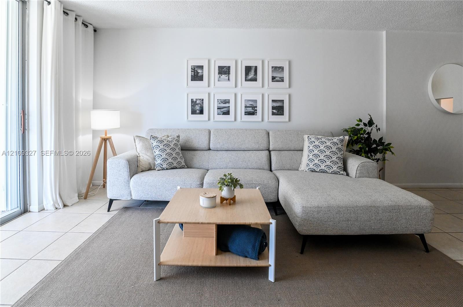 Living space featuring large format light-toned floor tiling, textured ceiling, and sliding glass door with full-height window panels