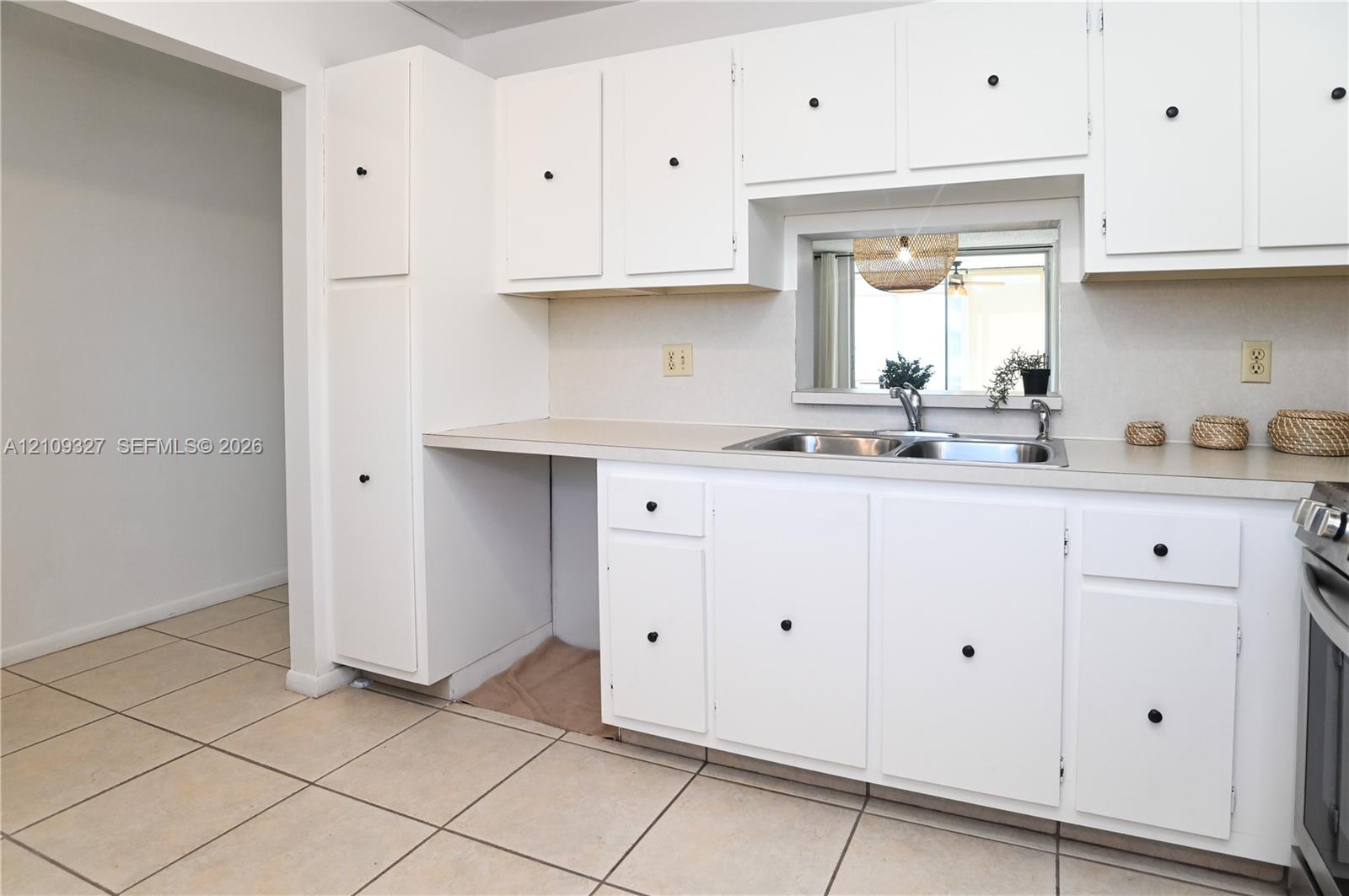 Kitchen featuring white cabinetry, a double-basin stainless steel sink, neutral countertop, and tiled flooring