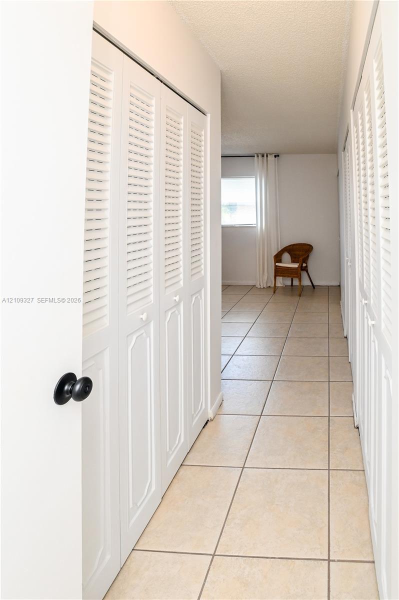 Hallway featuring ceramic tile flooring and multiple sets of white louvered-style closet doors