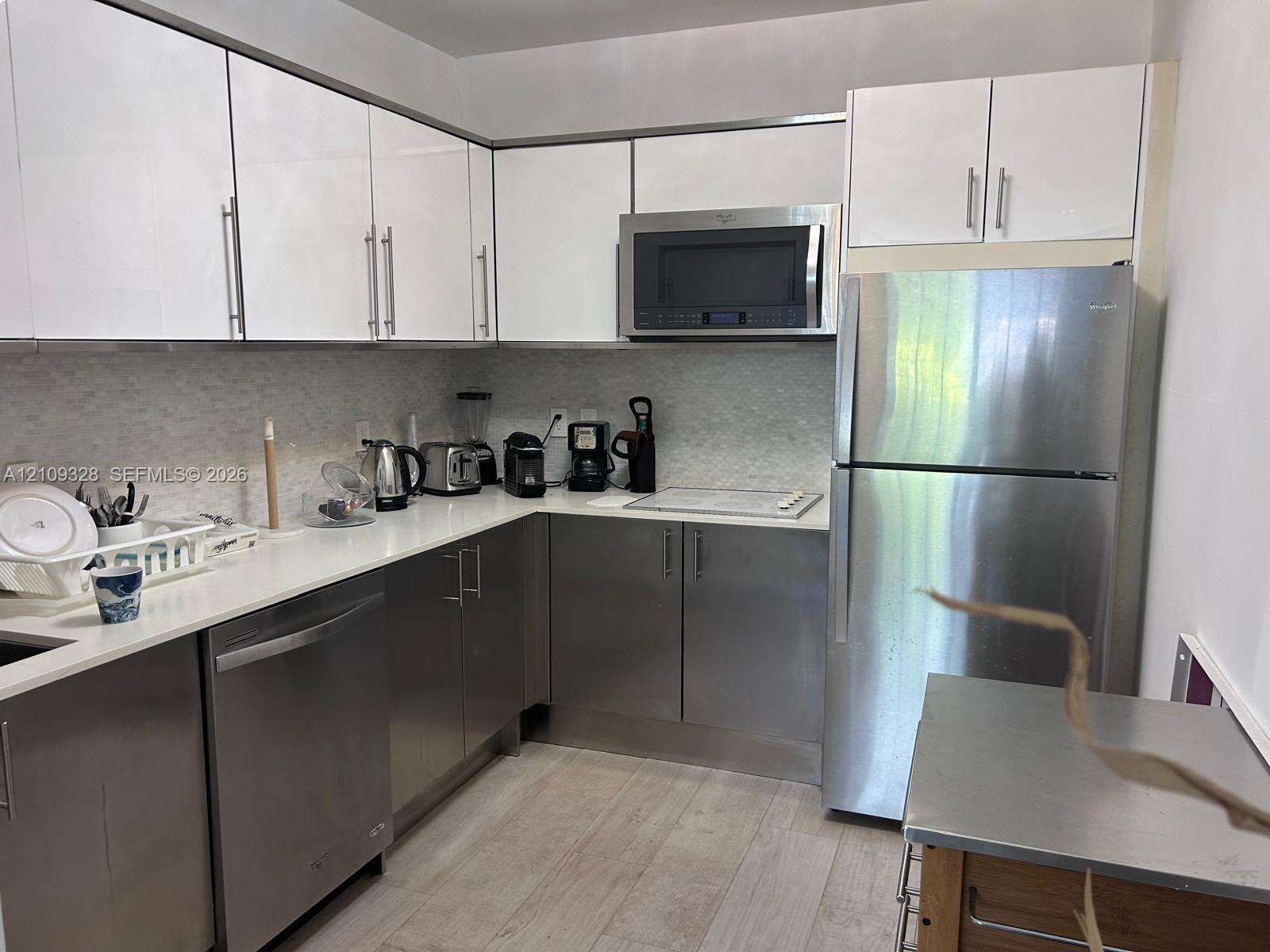 Kitchen featuring white upper cabinetry, stainless steel lower cabinets, light-toned countertop, textured backsplash, and stainless steel appliances