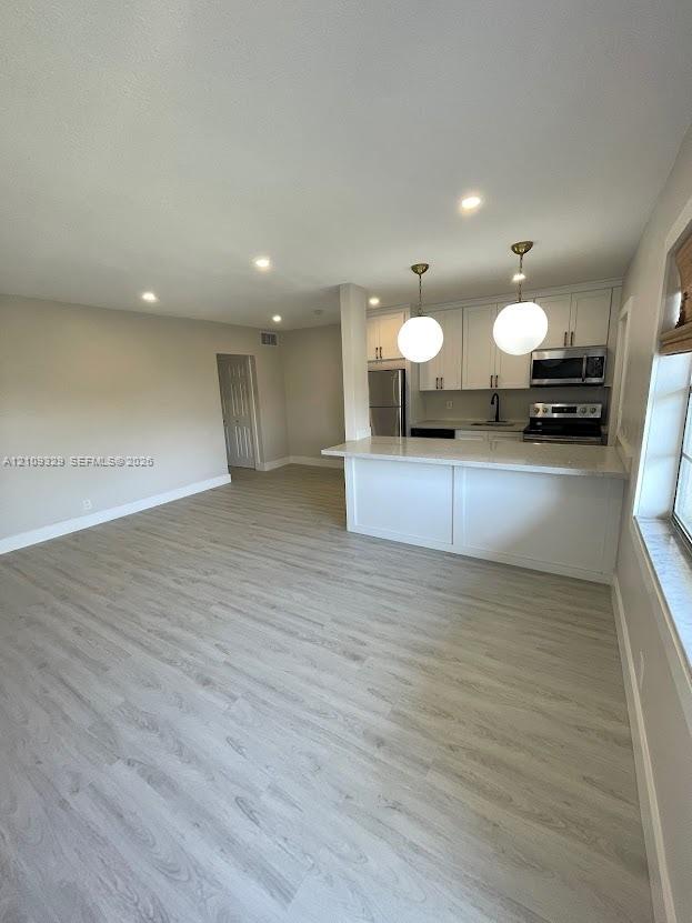 Kitchen featuring white cabinetry, a breakfast bar with stone-finish countertop, recessed lighting, and dual globe pendant lights, complemented by wood-finish flooring