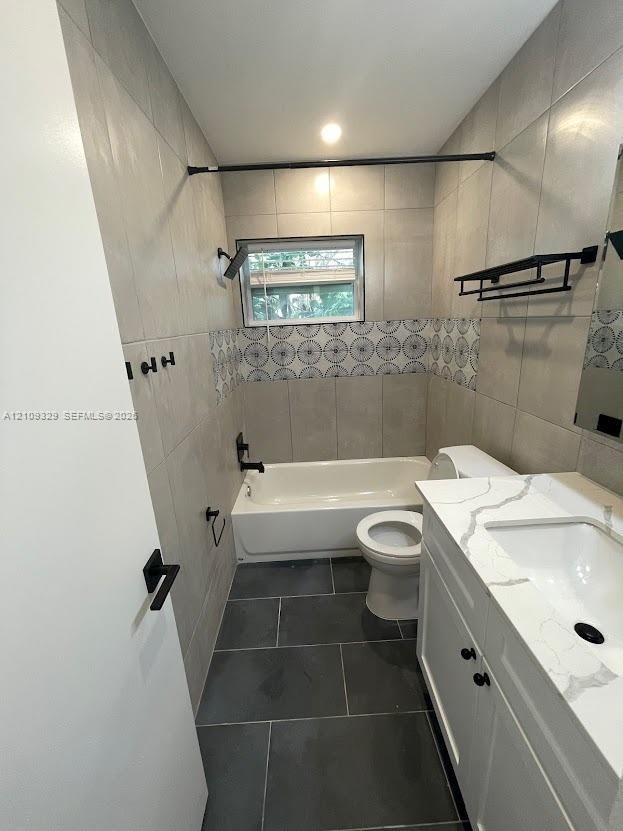Bathroom featuring a white vanity with a quartz-style countertop, large-format tile flooring, a shower-tub combination with patterned accent tiling, and matte black fixtures