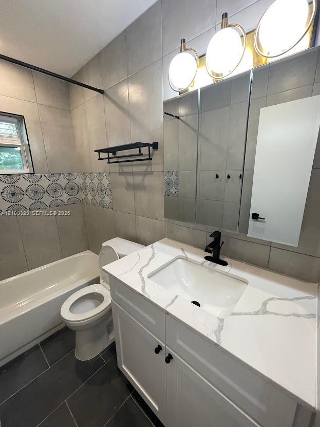 White cabinetry vanity with a stone-composite countertop, matte black faucet, wall-mounted medicine cabinet with integrated lighting, and decorative tile accent wall