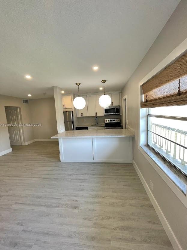 Kitchen featuring a peninsula with white cabinetry, quartz-style countertops, dual globe pendant lighting, and stainless steel appliances, set against wood-finish flooring
