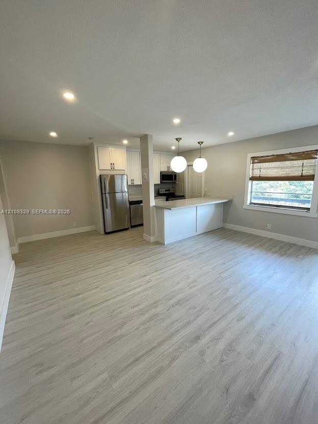 Kitchen featuring white cabinetry, wood-finish flooring, stainless steel appliances, a breakfast bar, and pendant lighting