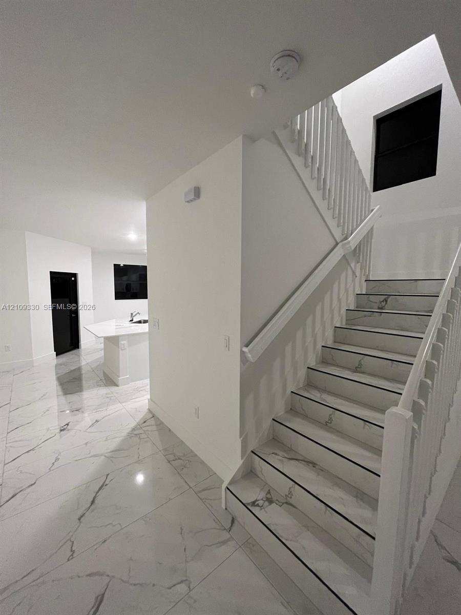 Staircase featuring white balusters and stone-finish treads, complemented by extensive stone-finish floor tiling and a kitchen island with a stone-finish countertop
