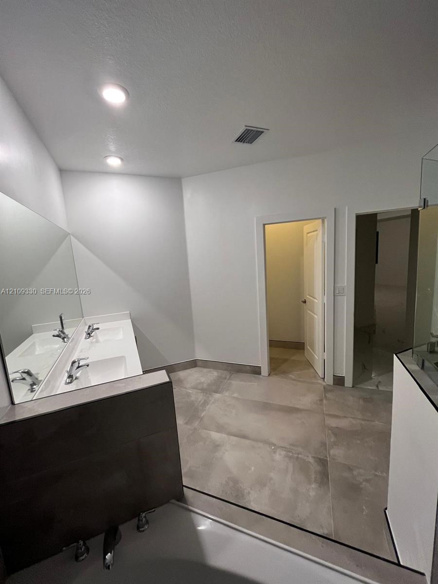 Dual-sink vanity with a large wall-mounted mirror, recessed ceiling lighting, and expansive floor tiling