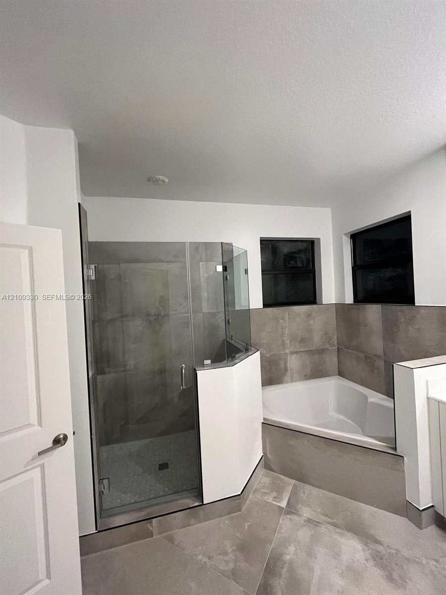 Bathroom featuring a glass-enclosed shower, built-in soaking tub, large-format tile surround, and matte-finish floor tile