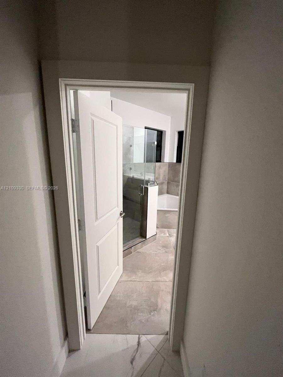 Bathroom interior featuring large-format tile flooring, a glass-enclosed shower, a soaking tub, and a multi-panel door