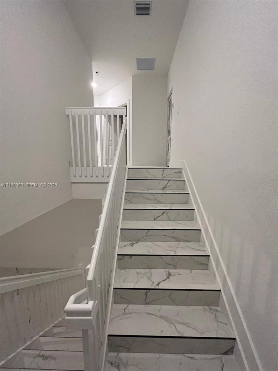 Staircase featuring white stone-patterned treads, white railing, and white balusters