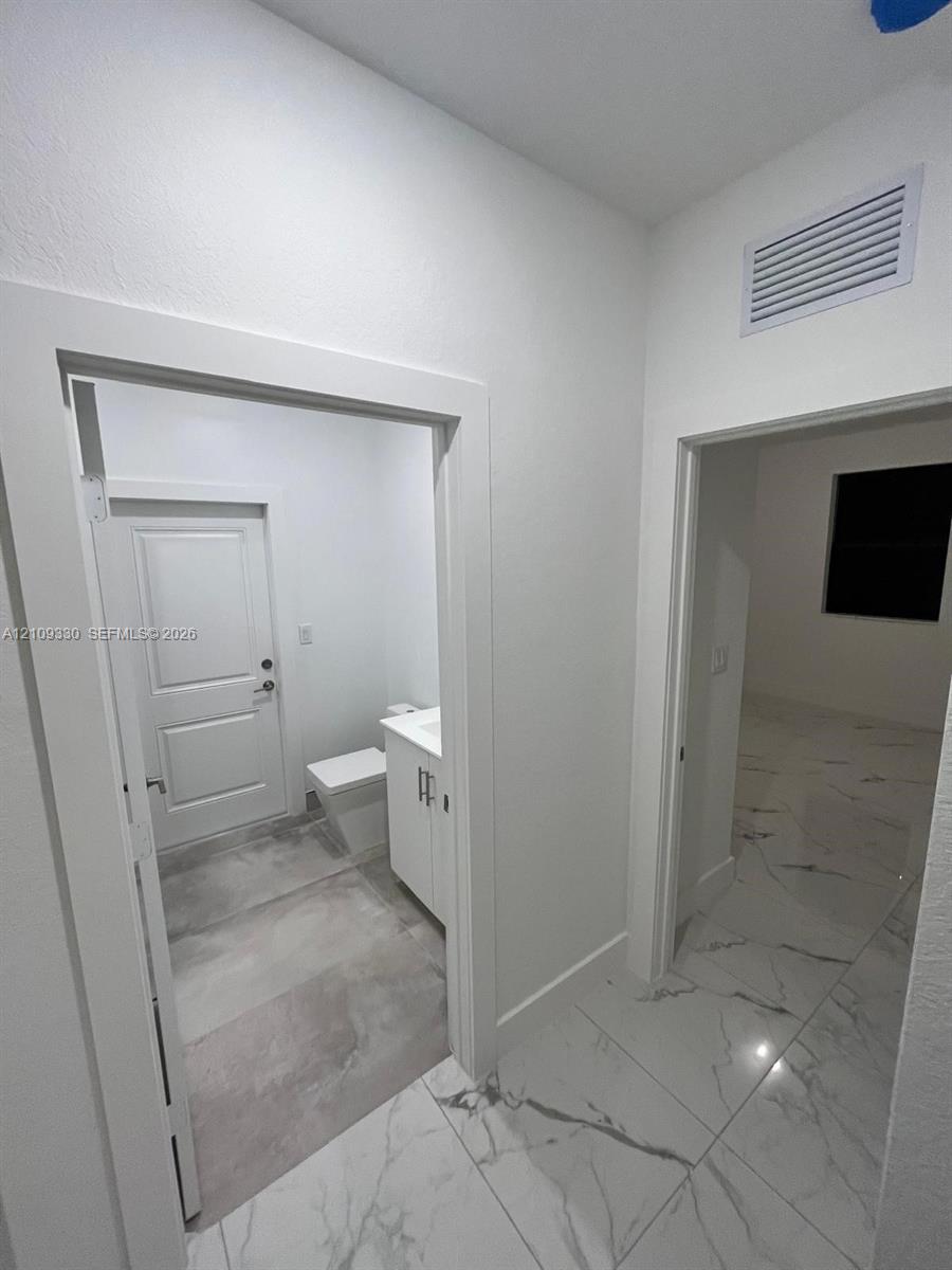 Large-format stone-style tile flooring with neutral veining, white shaker-style cabinetry, and solid-core interior doors