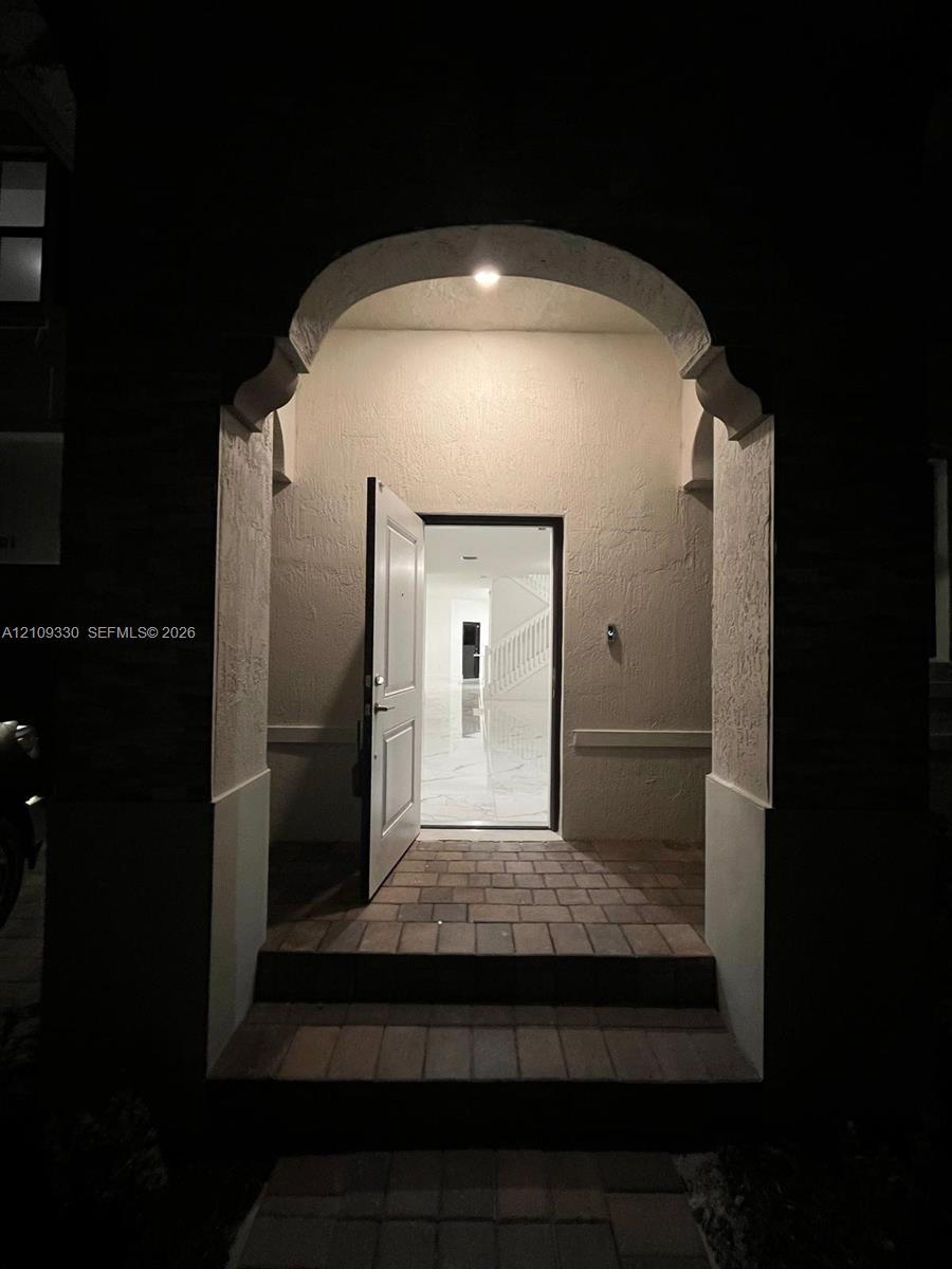 Covered entryway featuring a stone-paver stoop and an arched architectural opening with recessed lighting