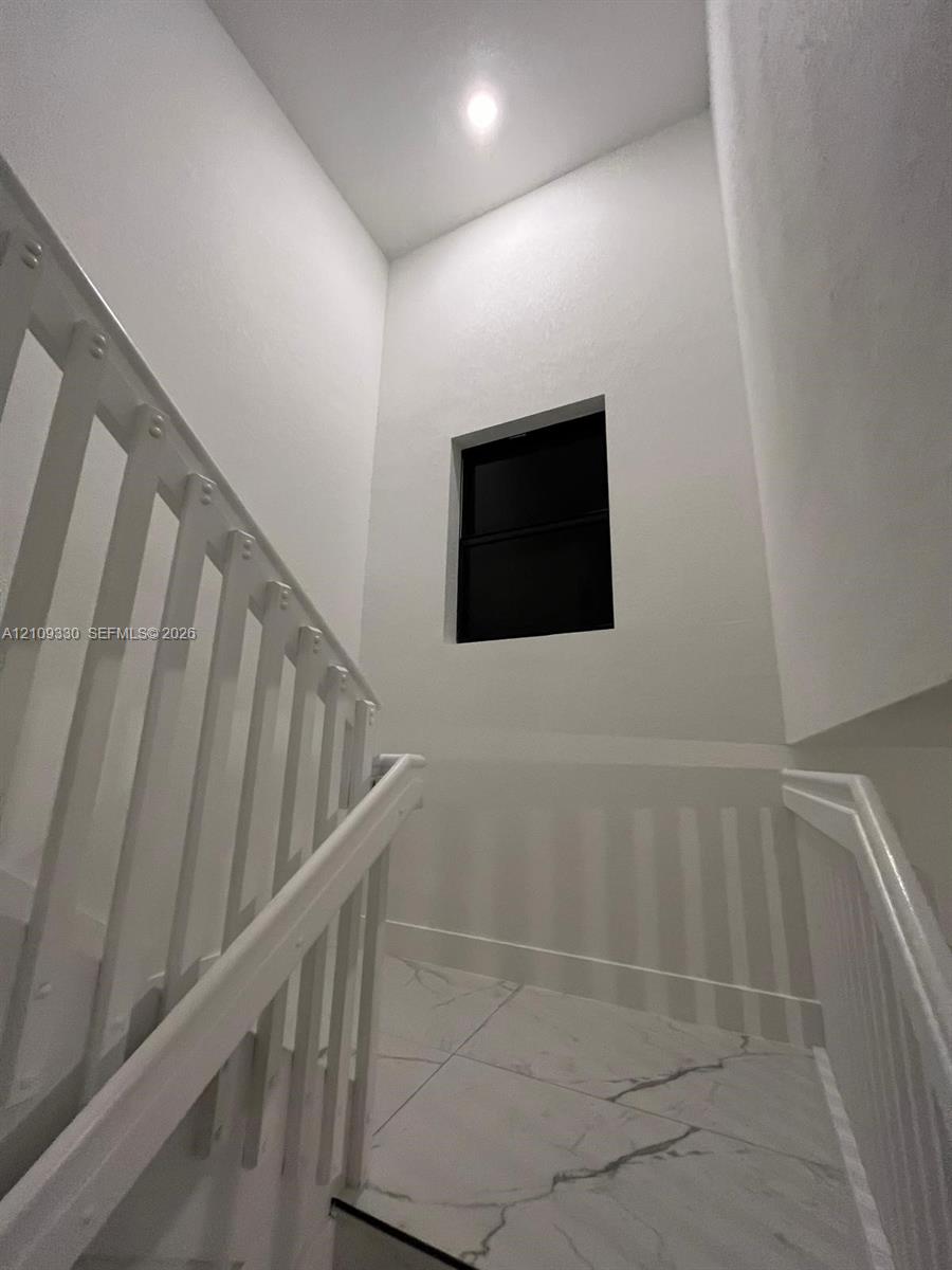 Stairwell featuring white vertical balusters, light-colored tile flooring with distinctive veining, recessed ceiling lighting, and a square window