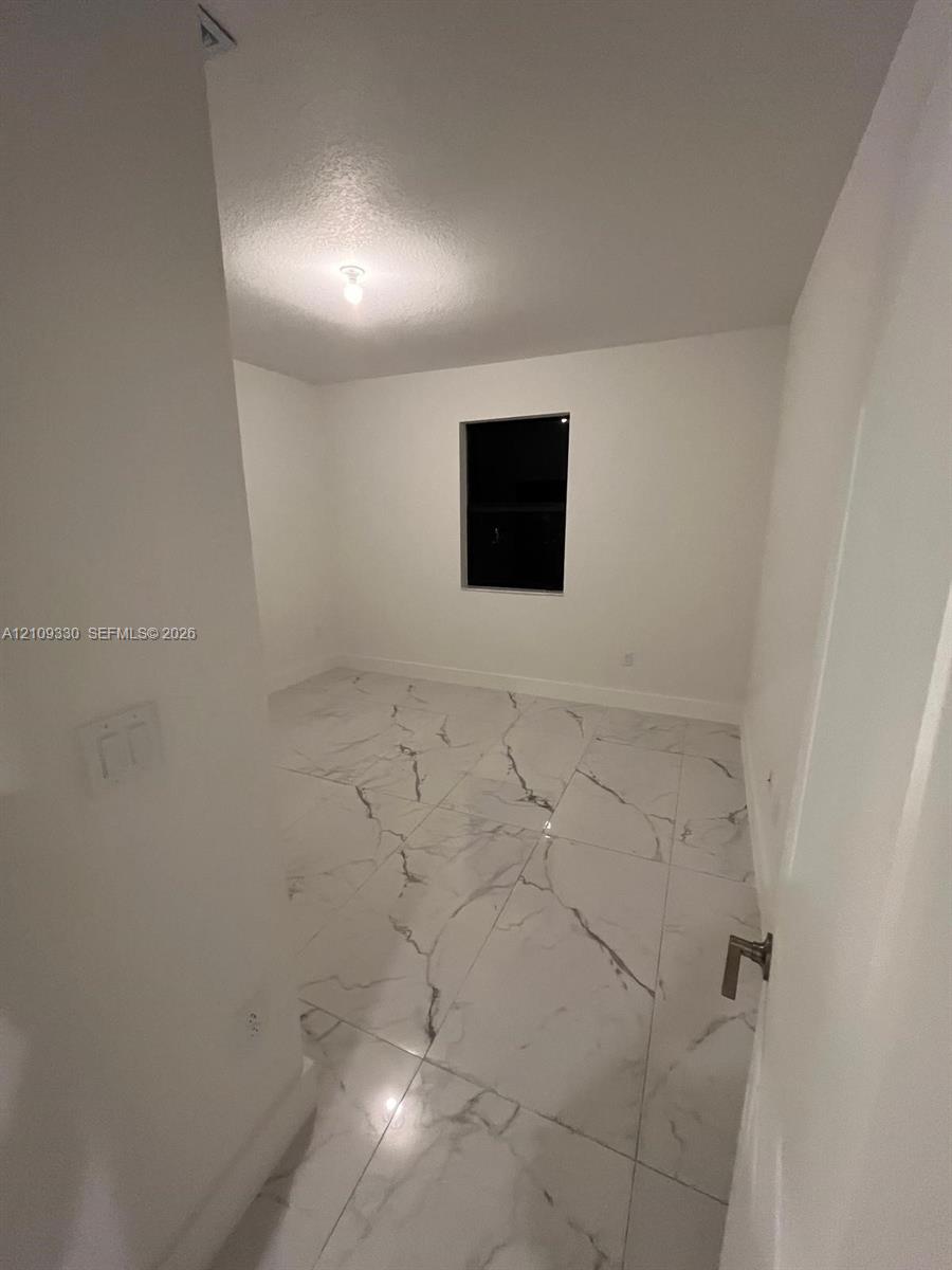 Interior space featuring large-format white stone-finish flooring with dark veining, neutral wall paint, and a single-pane window