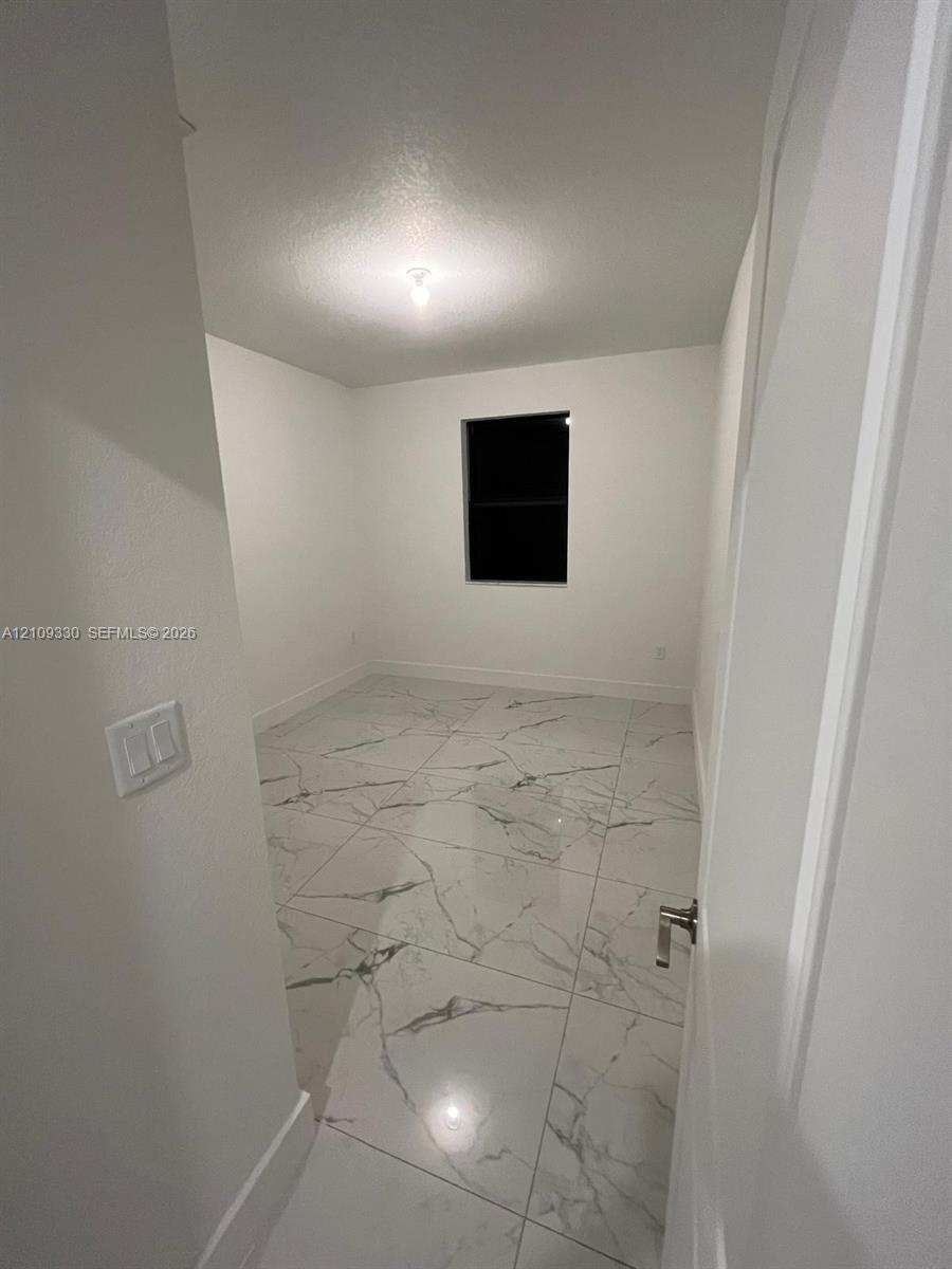 Interior space featuring large-format stone-finish floor tiling, neutral wall paint, and a single-pane window