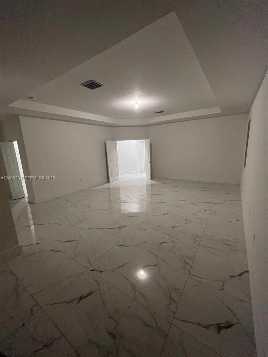 Tray ceiling, large-format stone-finish flooring with neutral veining, and double-door entry