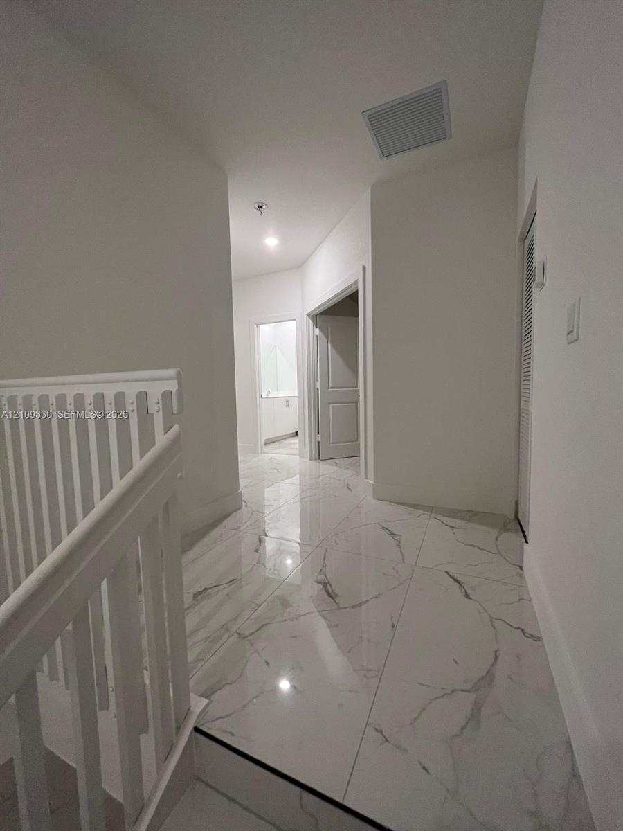 Large-format tile flooring with a veined pattern, white painted walls, and white wooden stair railing with vertical balusters