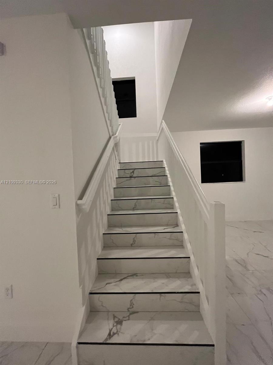Staircase featuring white stone-finish treads with grey veining, a painted white handrail, and white balusters