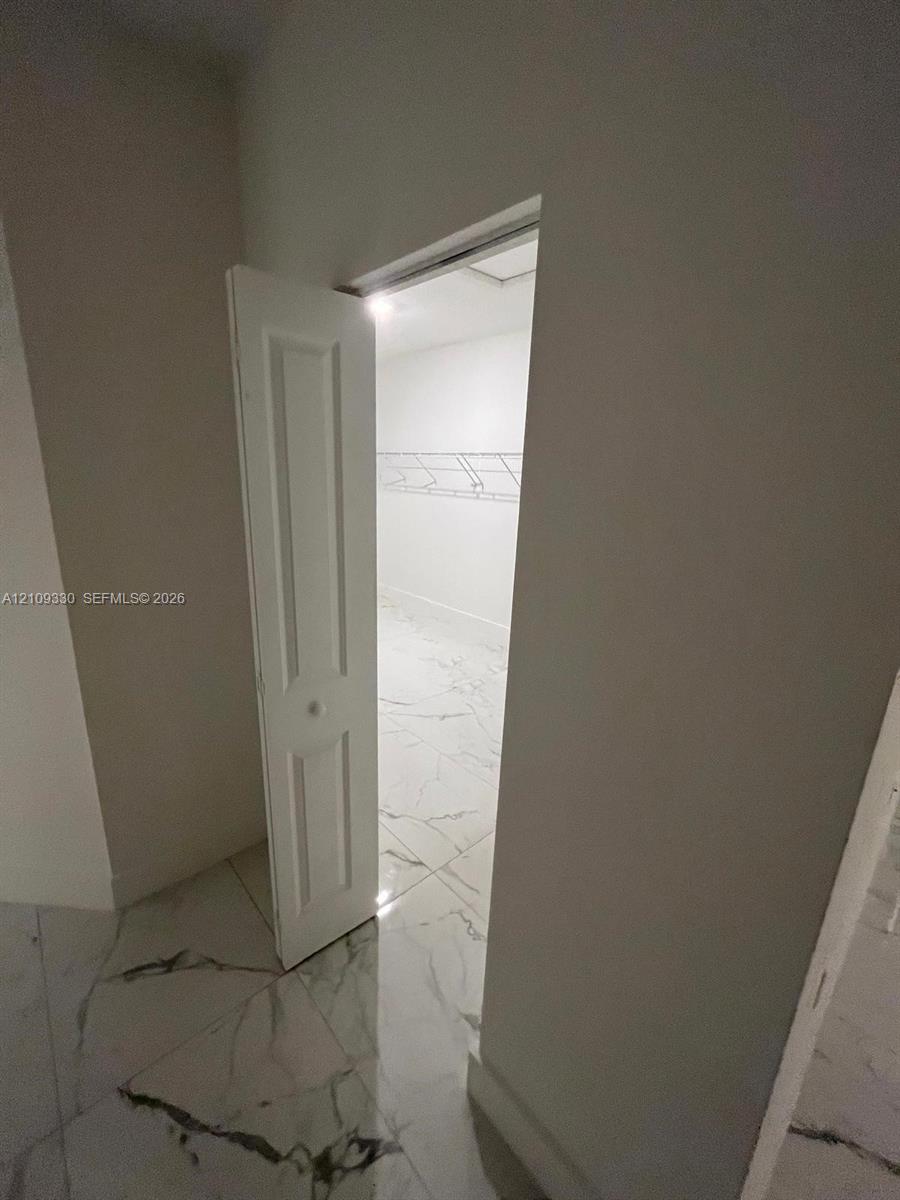 Storage space featuring white, six-panel bi-fold doors, white wire shelving, and large-format tile flooring with marble-pattern veining