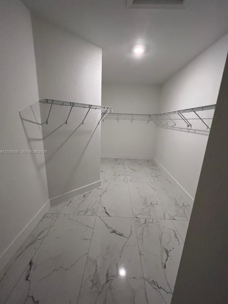 Walk-in closet featuring large-format tile flooring with a neutral veined pattern, white walls, and tiered metal wire shelving