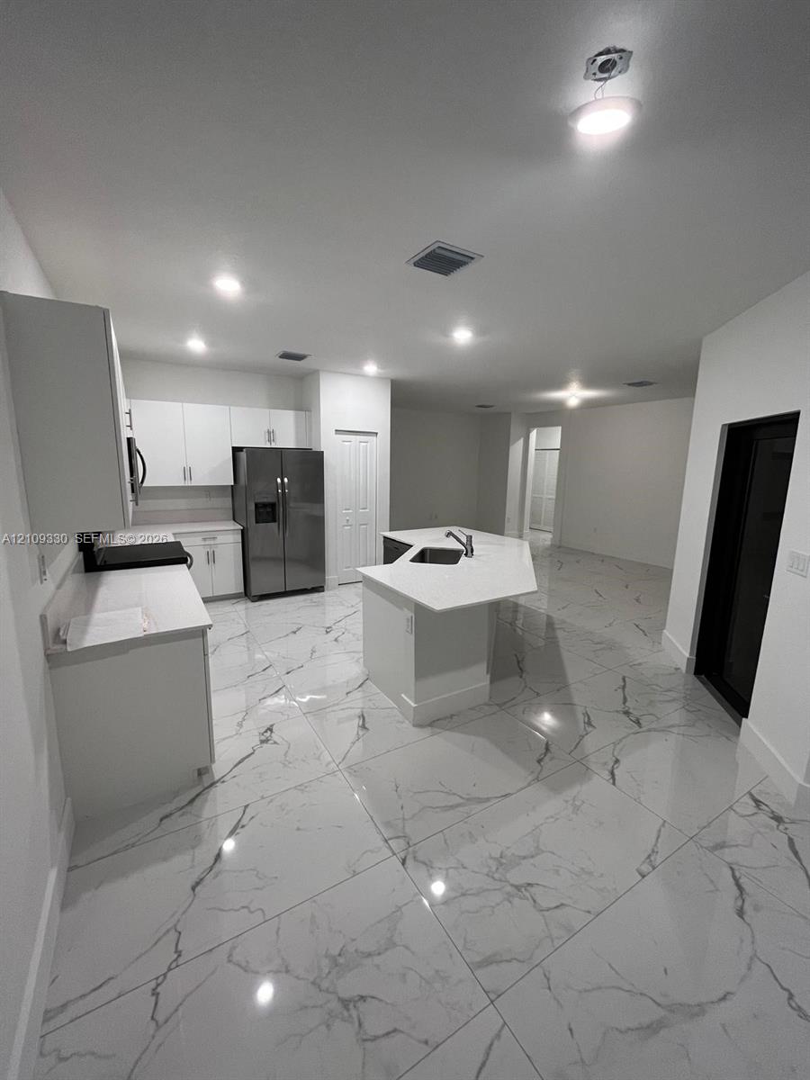 Kitchen featuring white cabinetry, center island with stone-finish countertops, stainless steel appliances, and large-format porcelain tile flooring