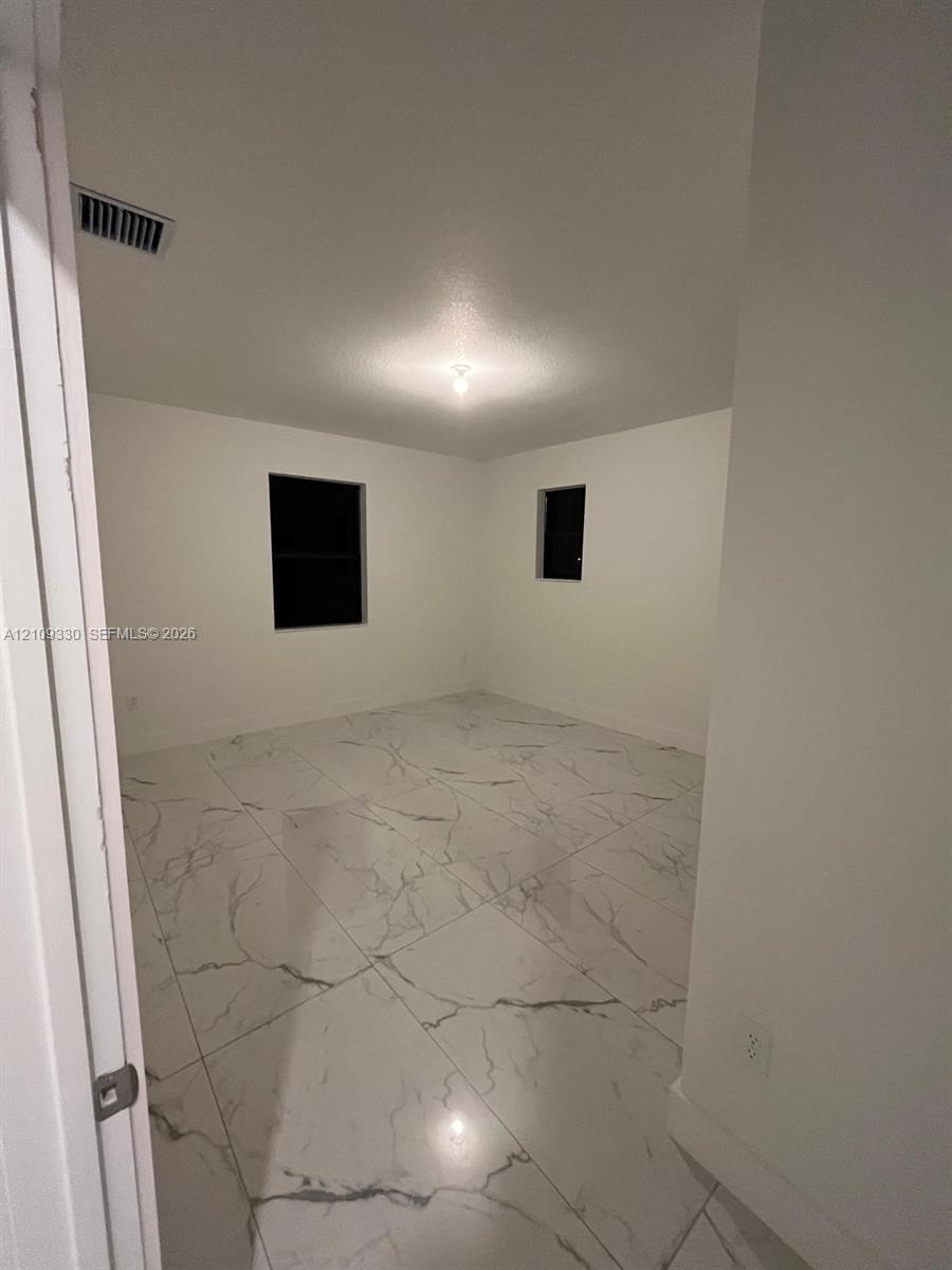 Room featuring large-format white tile flooring with grey veining, neutral wall tones, and two windows