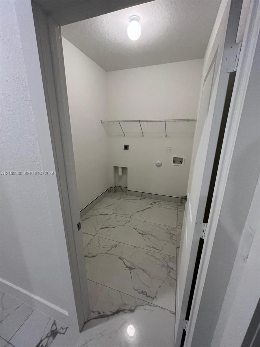 Utility space featuring large-format tile flooring with a neutral veining pattern, built-in wire shelving, and dedicated washer and dryer hookups