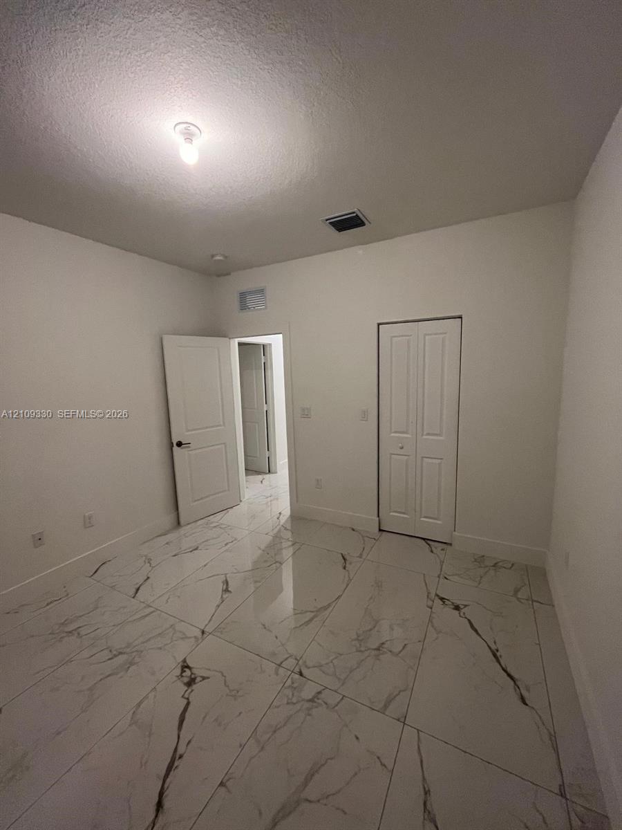 Large-format stone-patterned tile flooring, neutral wall finishes, white six-panel interior doors, and a double-door closet