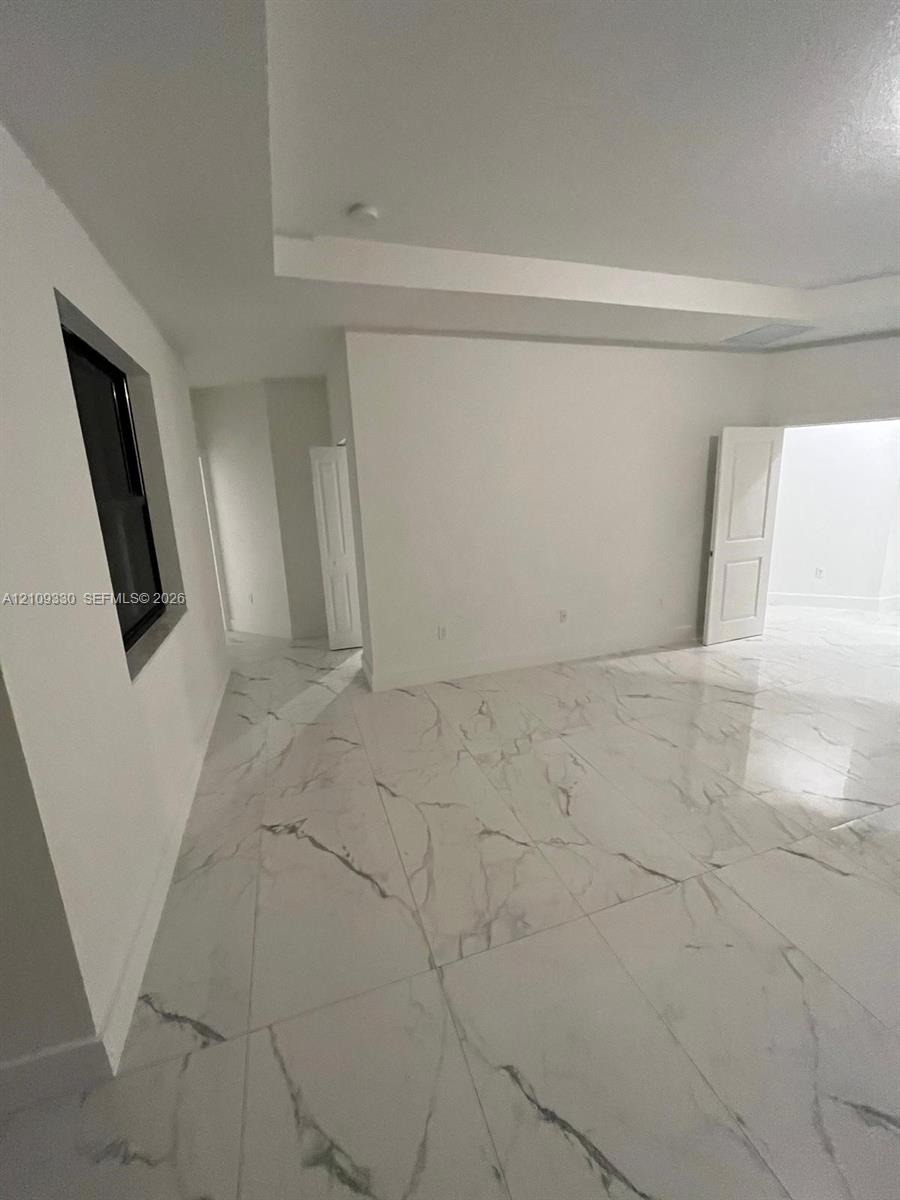 Large-format tile flooring with a marble-pattern finish, recessed tray ceiling, and white panel doors