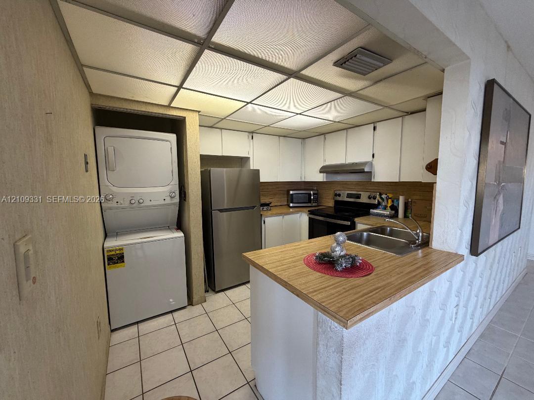 Kitchen featuring white cabinetry, wood-finish countertops, stainless steel appliances, a double-basin sink, and integrated laundry unit
