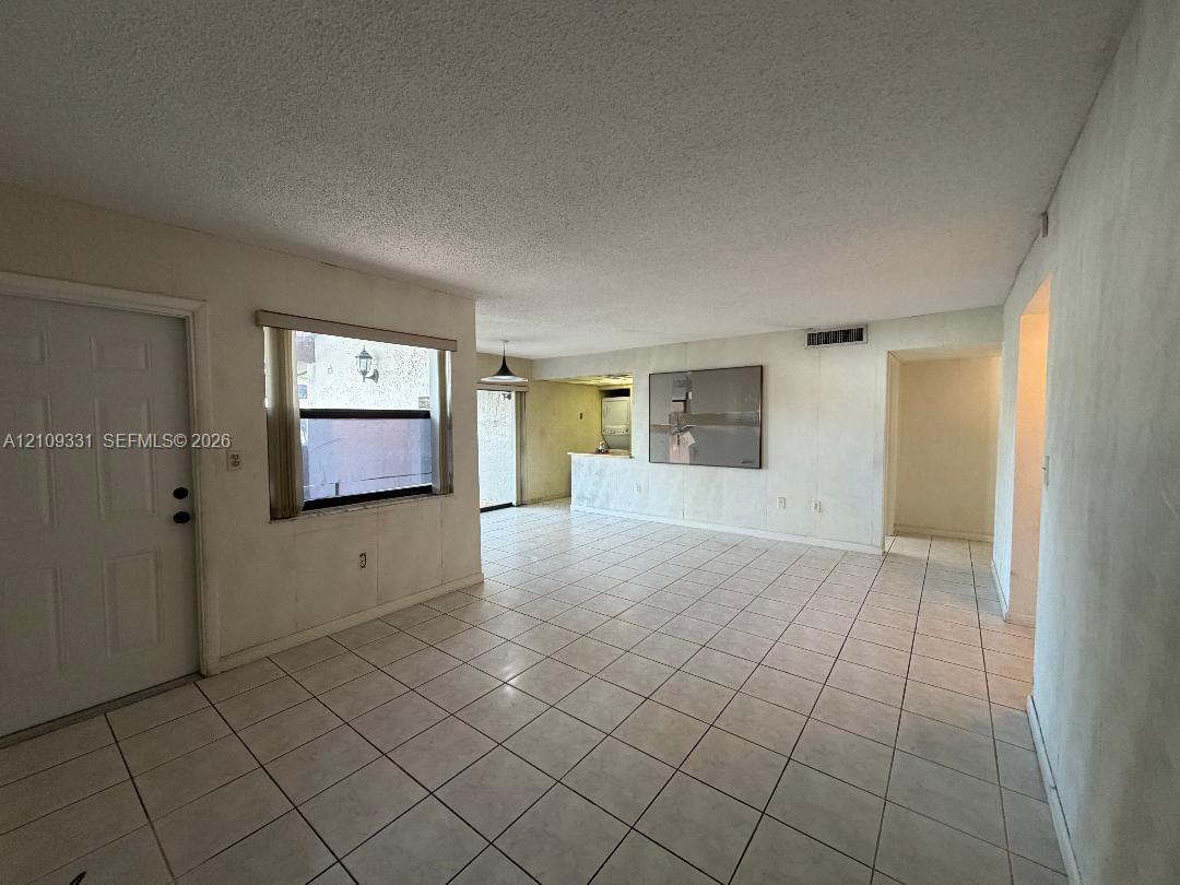 Open-concept interior featuring neutral ceramic tile flooring, a breakfast bar with stone-surface countertop, and a window with a horizontal blind